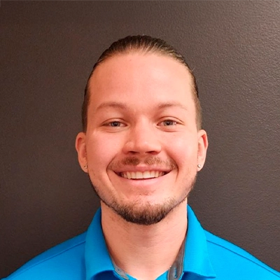 Person wearing a bright blue collared shirt standing against a plain dark wall