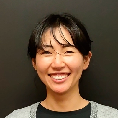Person wearing a light gray cardigan over a black shirt, standing against a plain dark background